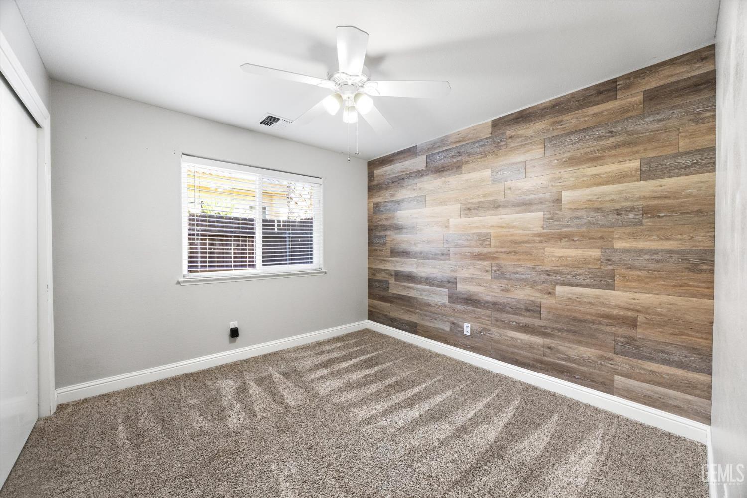 Empty bedroom with a wood-look plank accent wall, gray carpet, and a white ceiling fan.