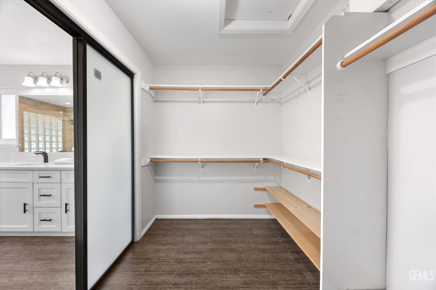 Walk-in closet with wood hanging rods, open shelving, and dark tile flooring.