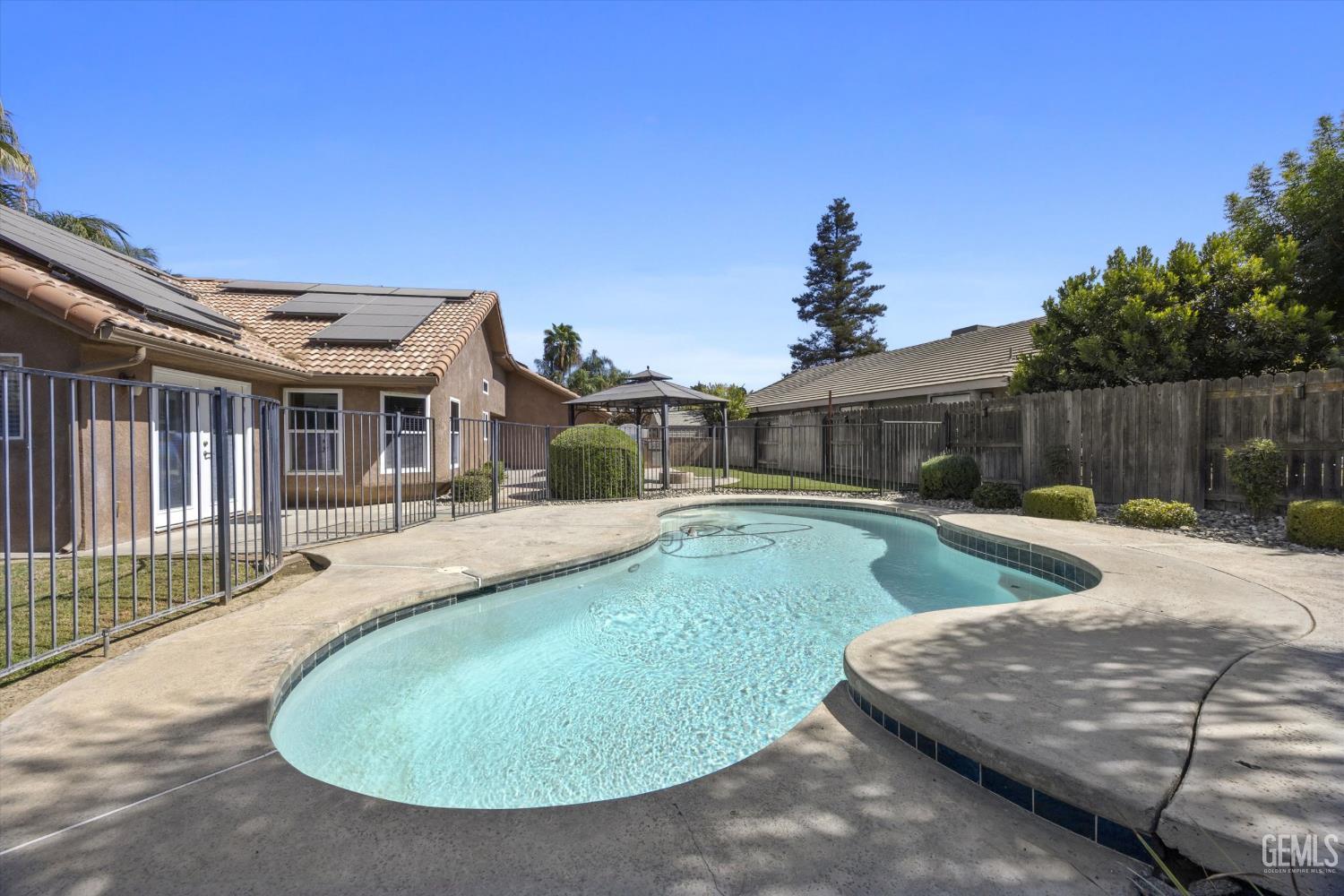 Backyard swimming pool with a curved shape, concrete patio, and metal safety fence.
