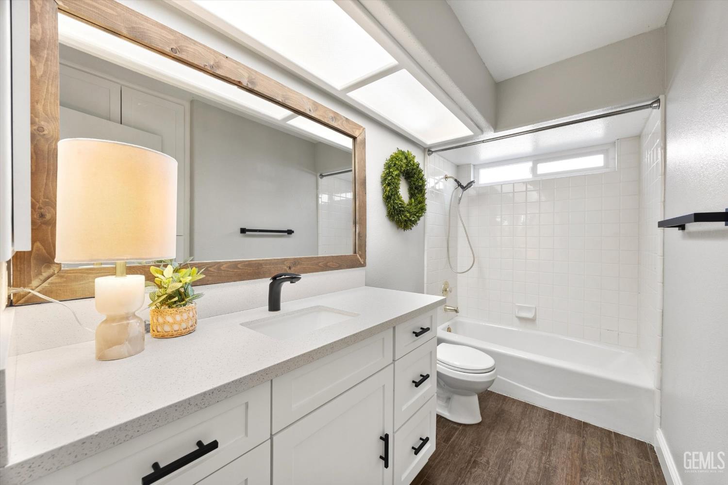 Bathroom with a white vanity and wood-framed mirror beside a tiled tub and shower.