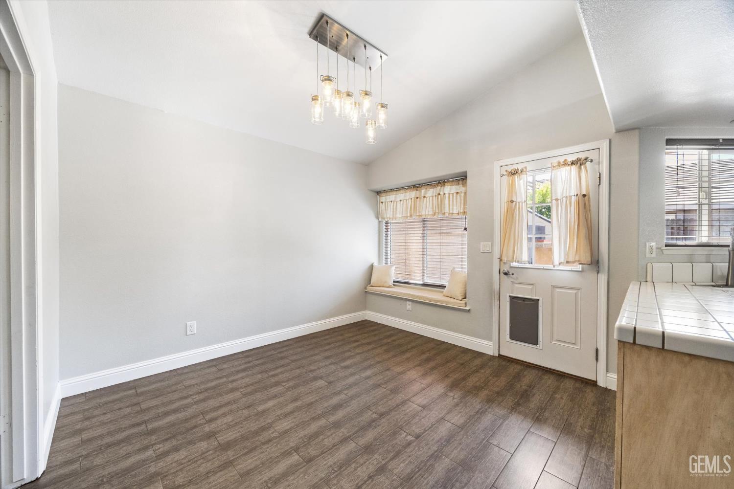 Empty dining area with wood-look flooring, a hanging light, window seat, and back door with pet door.