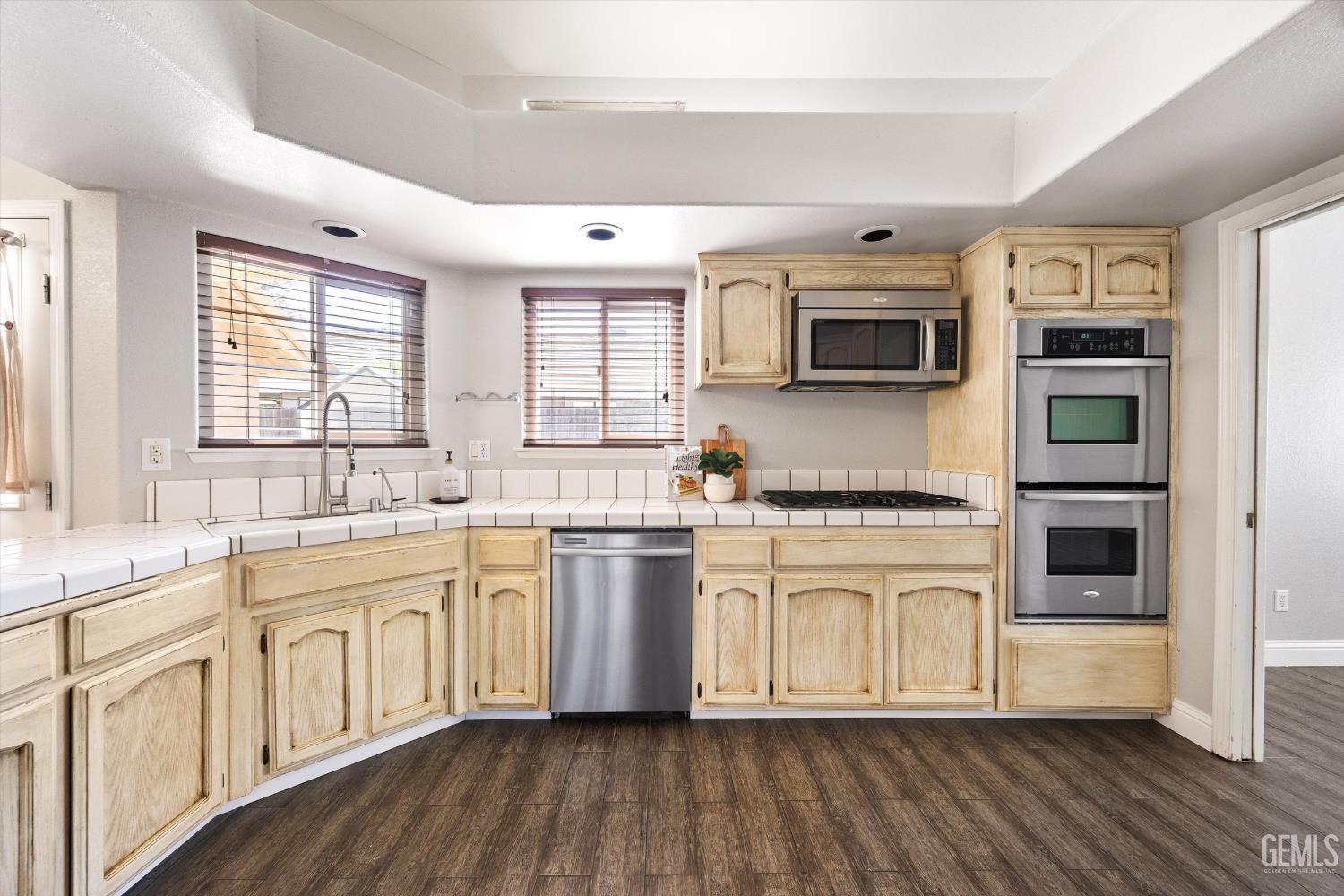 Kitchen with light wood cabinets, tiled counters, stainless steel appliances, and a gas cooktop.