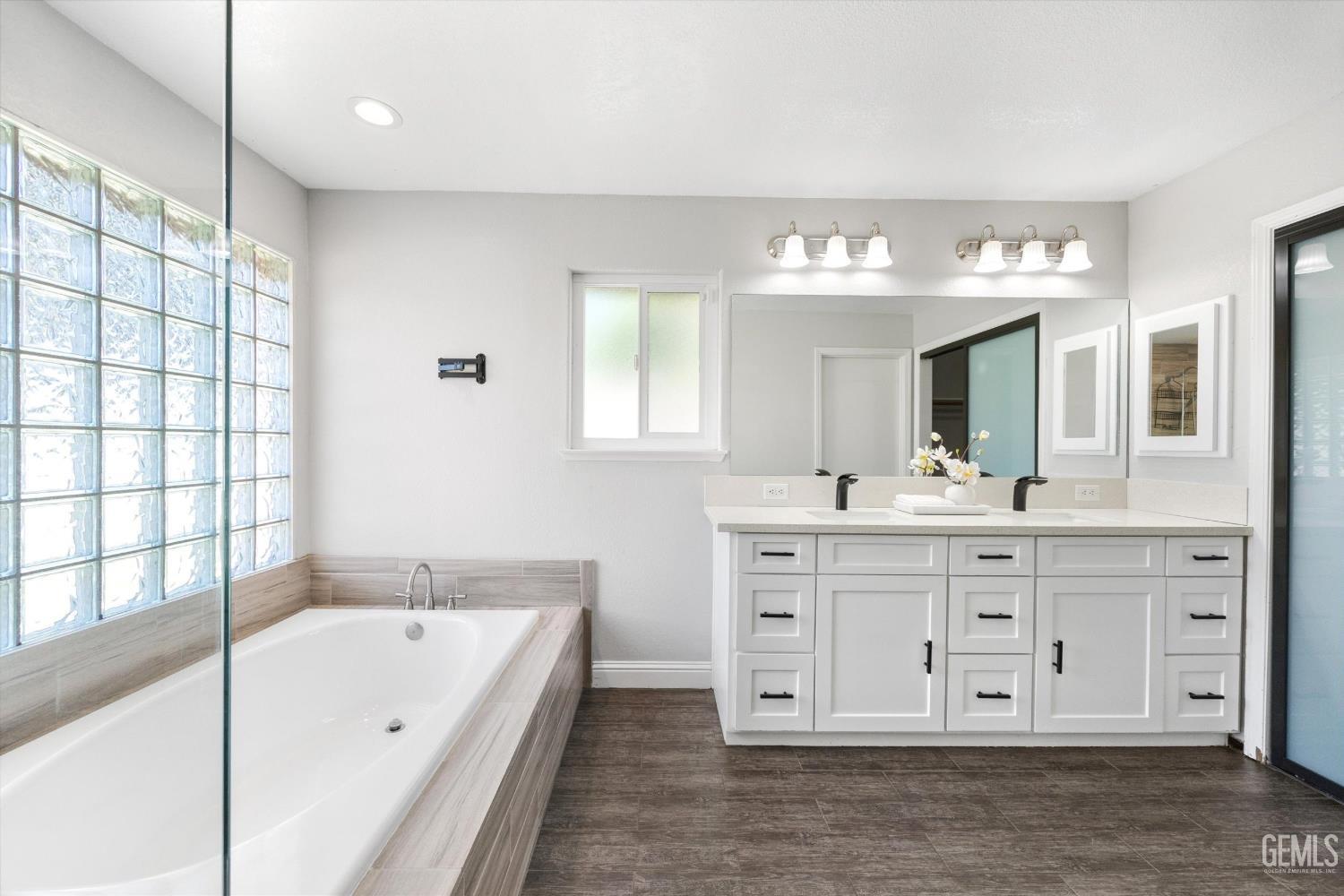 Bright bathroom with a soaking tub, glass-block windows, and a long white double vanity.