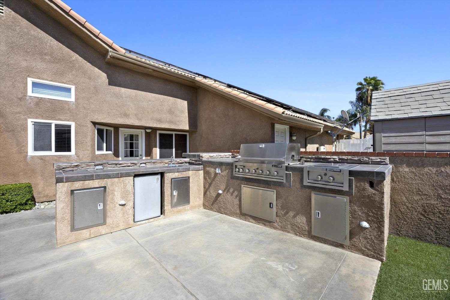 Outdoor kitchen with a built-in stainless-steel grill and stone-trimmed counters beside a stucco home.