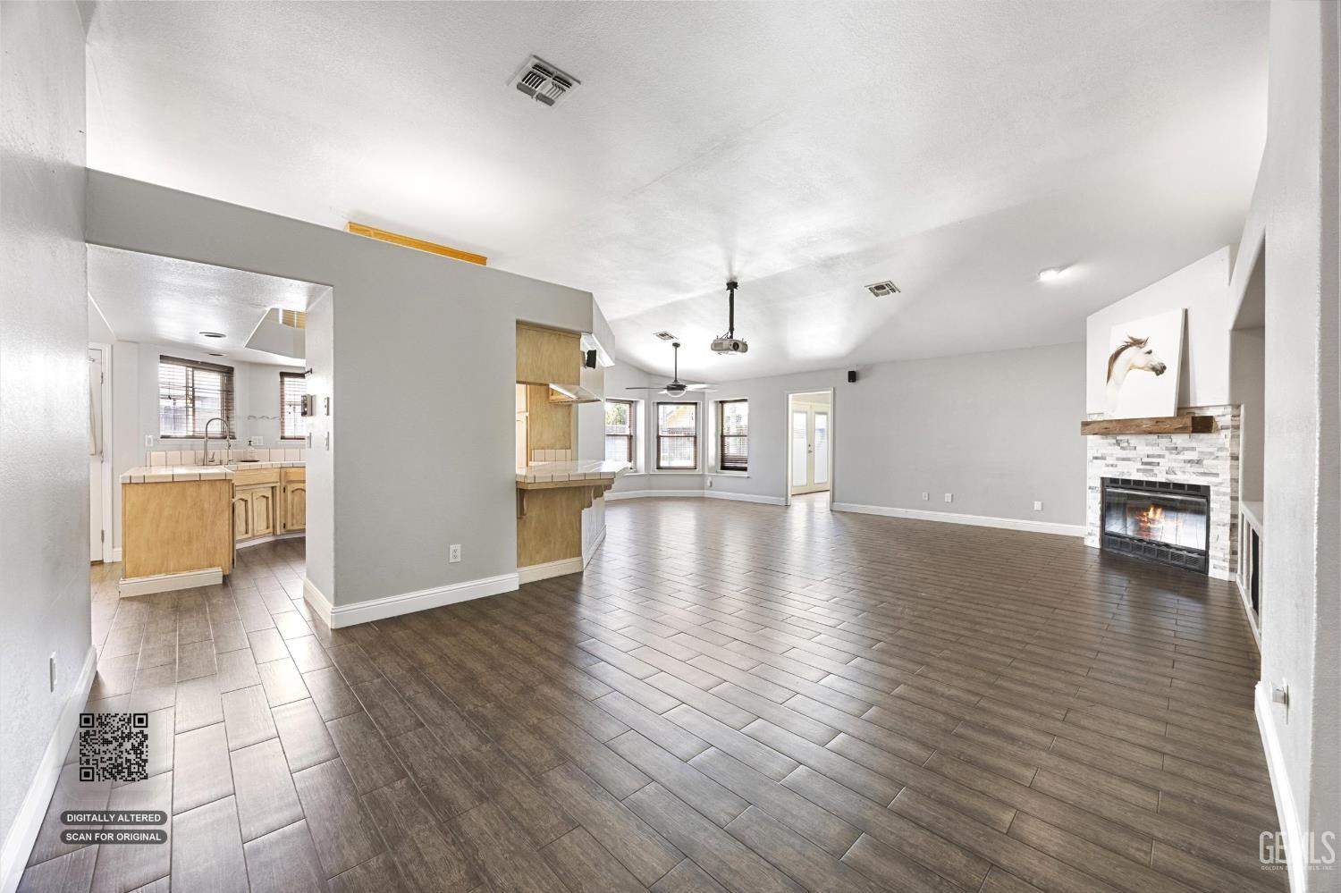 Open living room with dark tile flooring, a stone fireplace, and an adjoining kitchen.