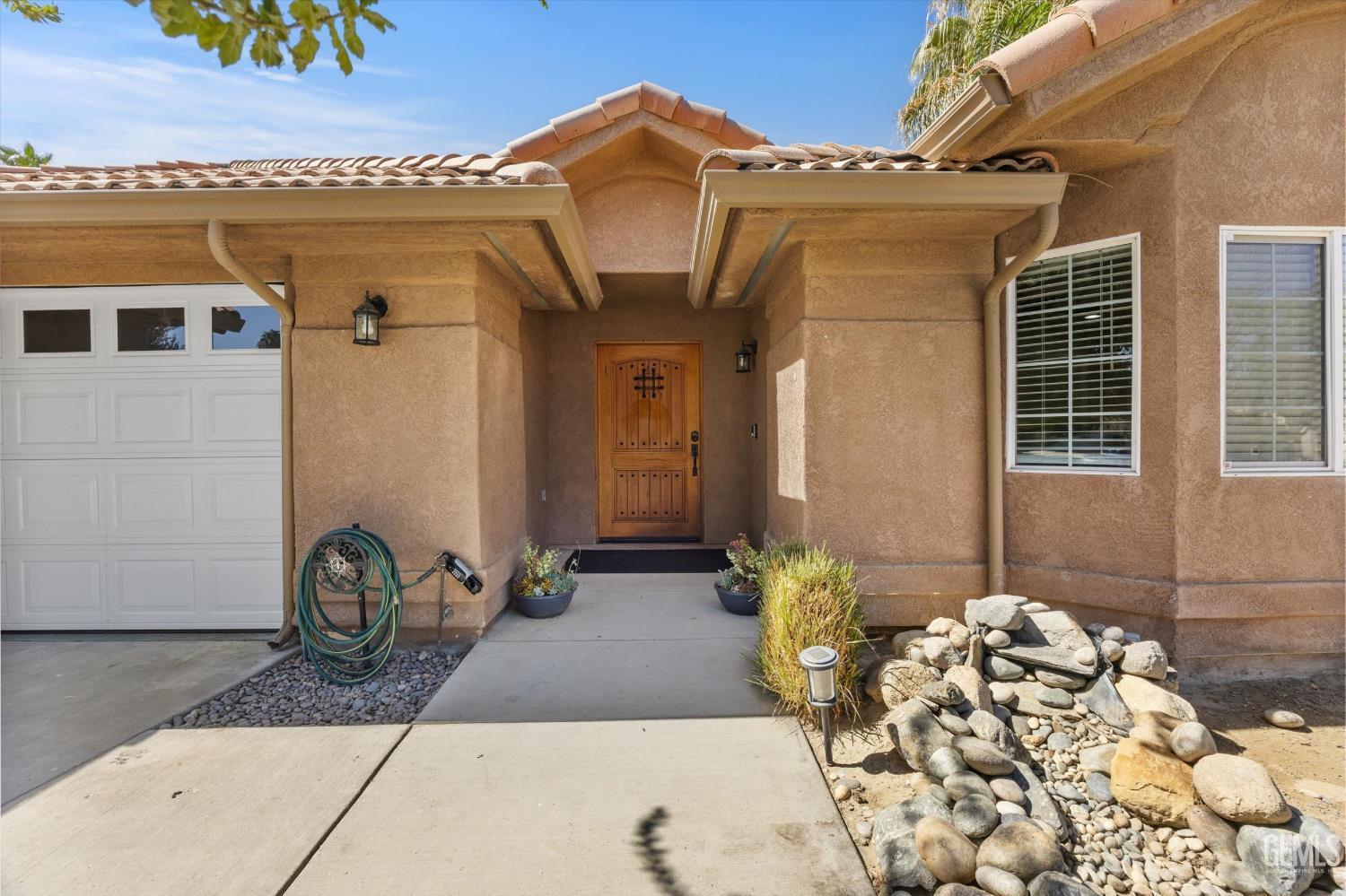 Home entrance with a wooden door, covered porch, white garage door, and rock landscaping.