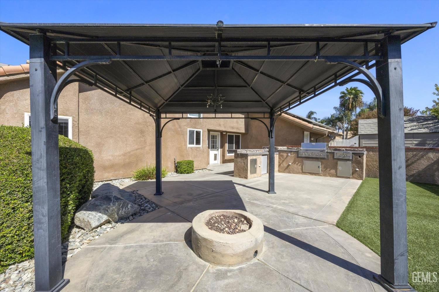 Covered backyard patio with an outdoor kitchen, circular fire pit, and spacious metal-roofed pavilion.