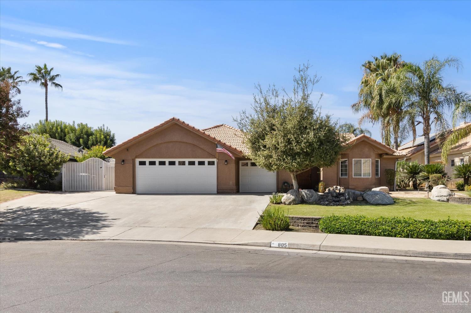 Single-story tan stucco home with two white garage doors, a wide driveway, and landscaped front yard.