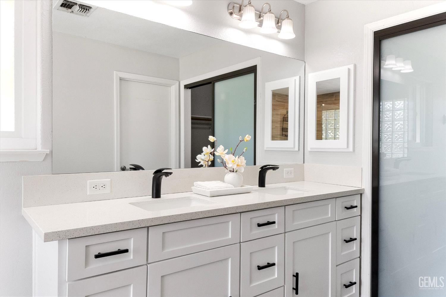 Bright bathroom with a white double vanity, black faucets, large mirror, and frosted-glass sliding doors.