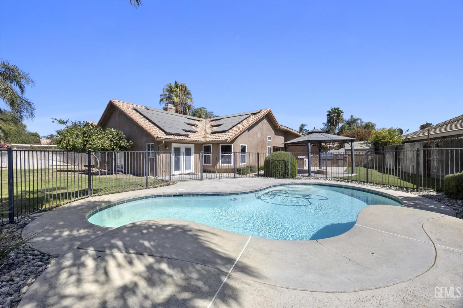 Backyard pool and patio behind a stucco home with solar panels.