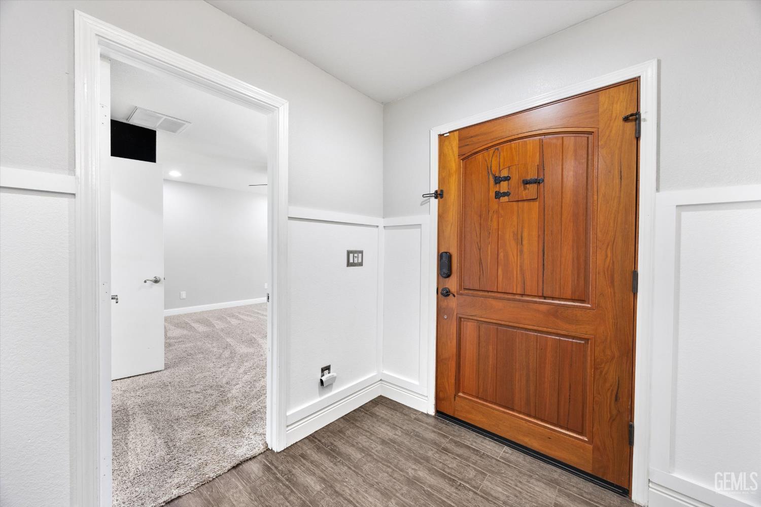 Entryway with a paneled wooden front door and an open doorway to a carpeted room.