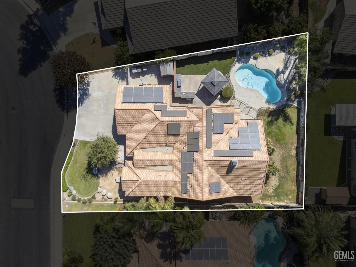 Aerial view of a tile-roofed home with solar panels, a backyard pool, and landscaped grounds.