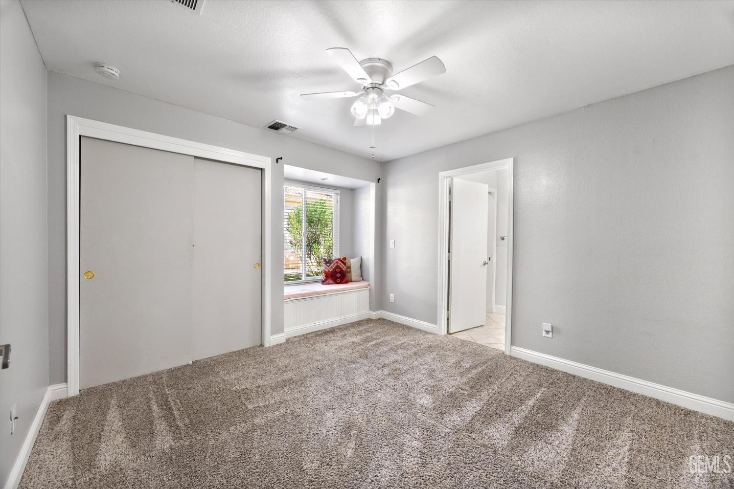 Bedroom with sliding closet doors, gray carpet, and a window seat overlooking greenery.
