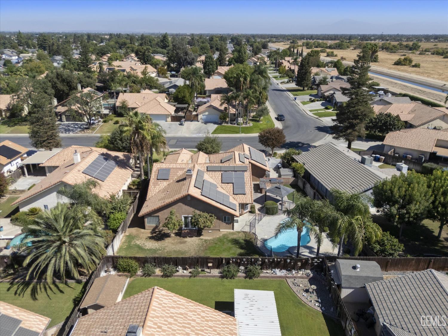 Aerial view of a home with rooftop solar panels and a backyard pool in a residential neighborhood.