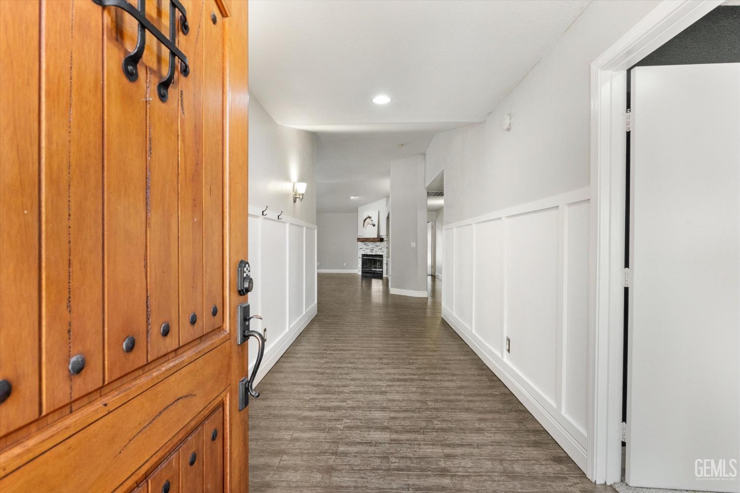 Entry hallway with a wooden front door, paneled walls, and plank flooring leading toward a fireplace.