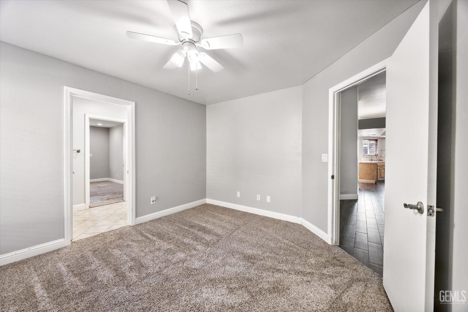 Unfurnished bedroom with plush carpet, a ceiling fan, and a doorway toward the kitchen.