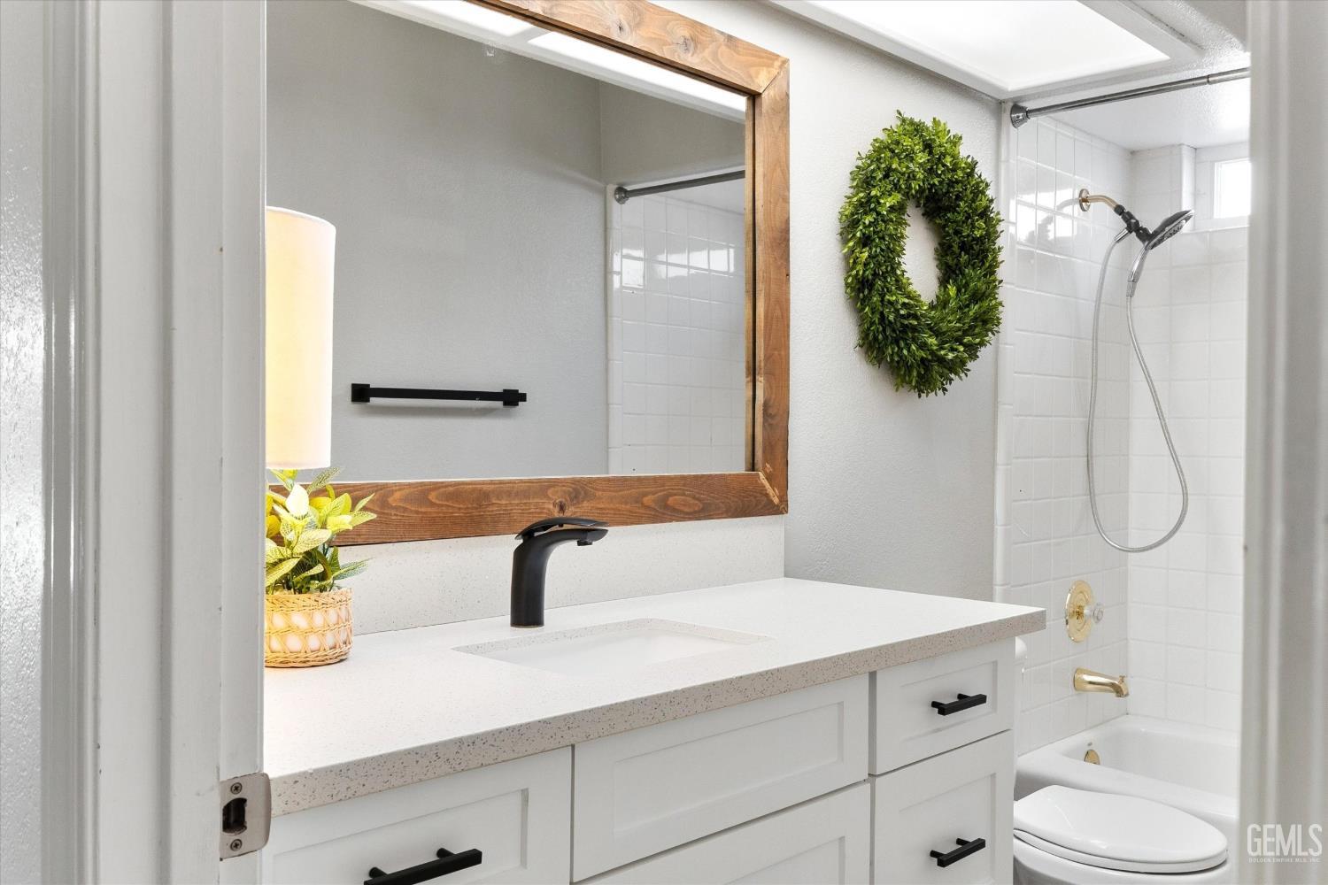 Bathroom with a white vanity, wood-framed mirror, and tiled tub and shower.