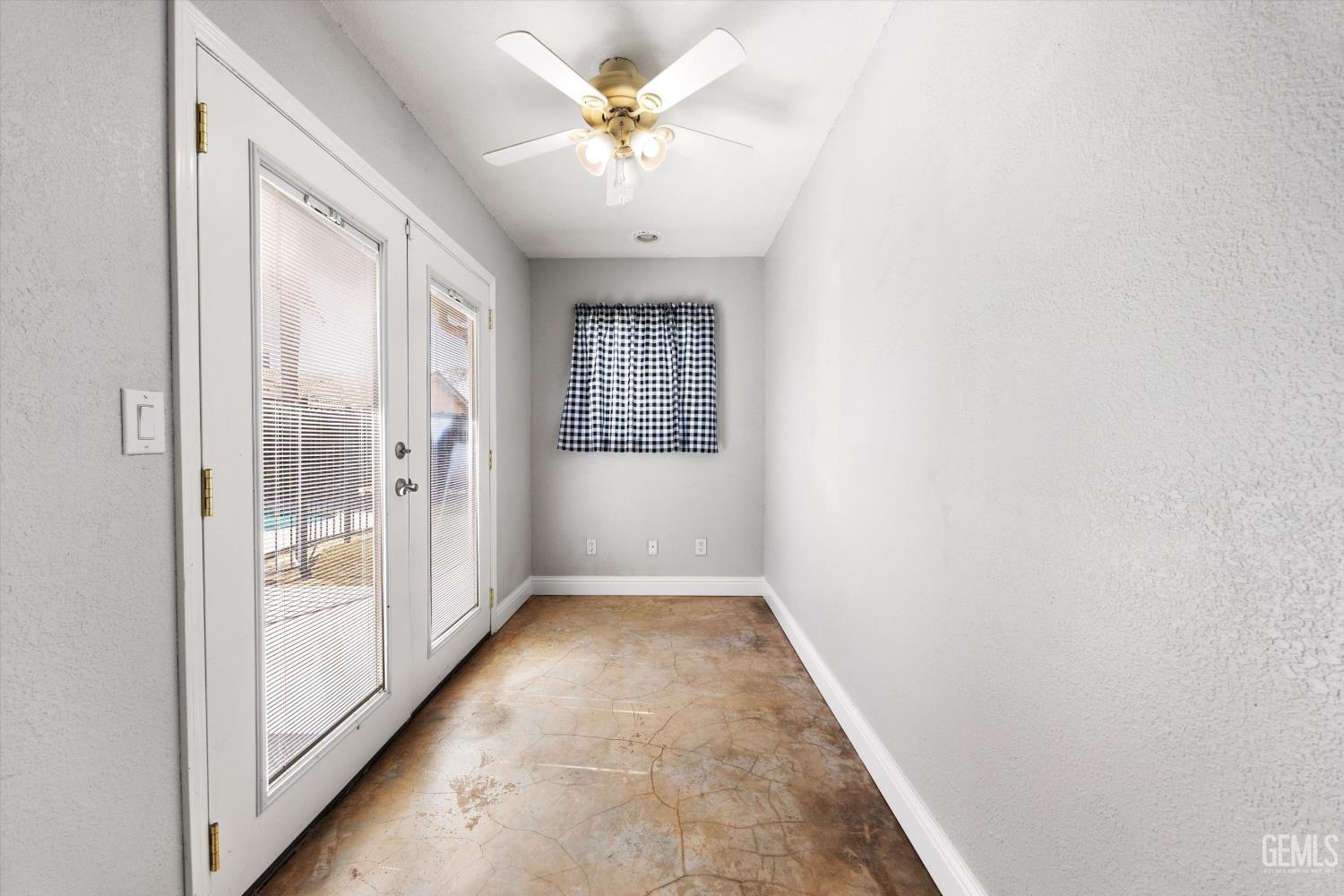 Bright sunroom with glass doors, a tan patterned floor, checkered curtain, and ceiling fan.