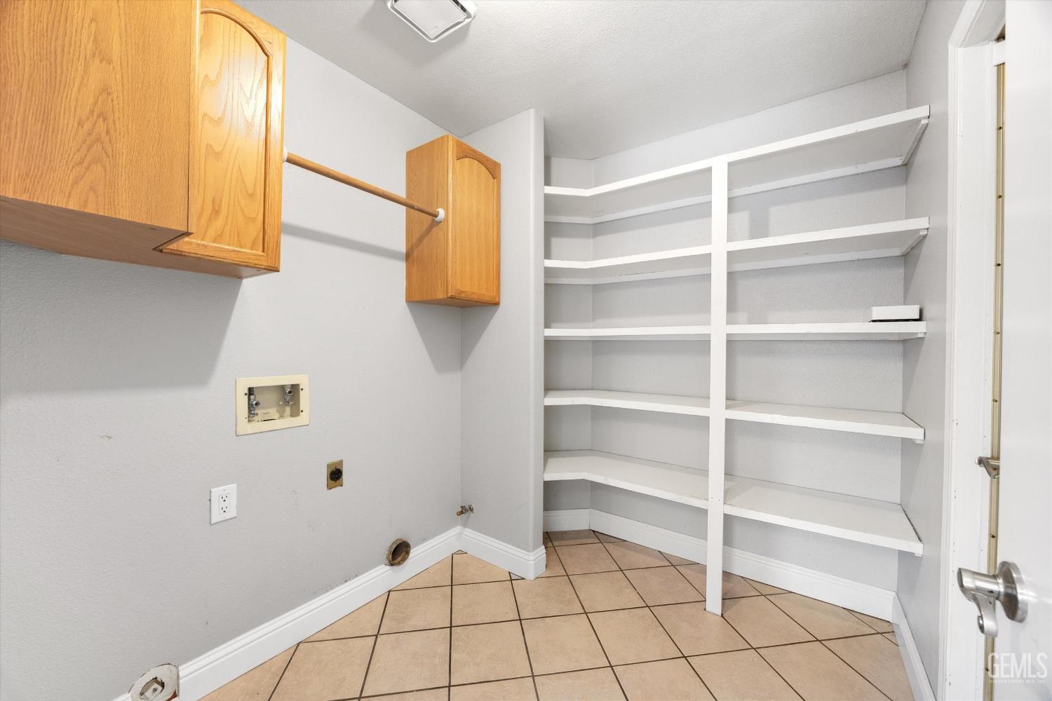 Empty laundry room with wood cabinets, washer connections, and extensive built-in shelving.