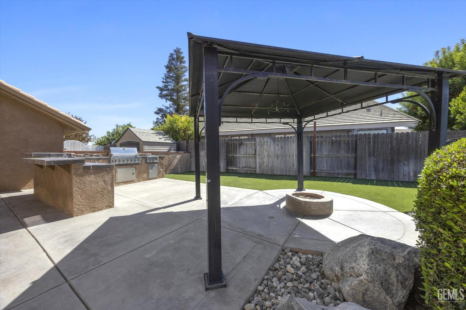 Backyard patio with a metal pergola, built-in grill, circular fire pit, and artificial turf.