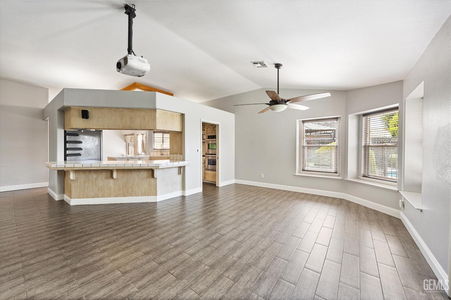 Vacant living area with tiled floors, a kitchen pass-through counter, two windows, and a ceiling-mounted projector.