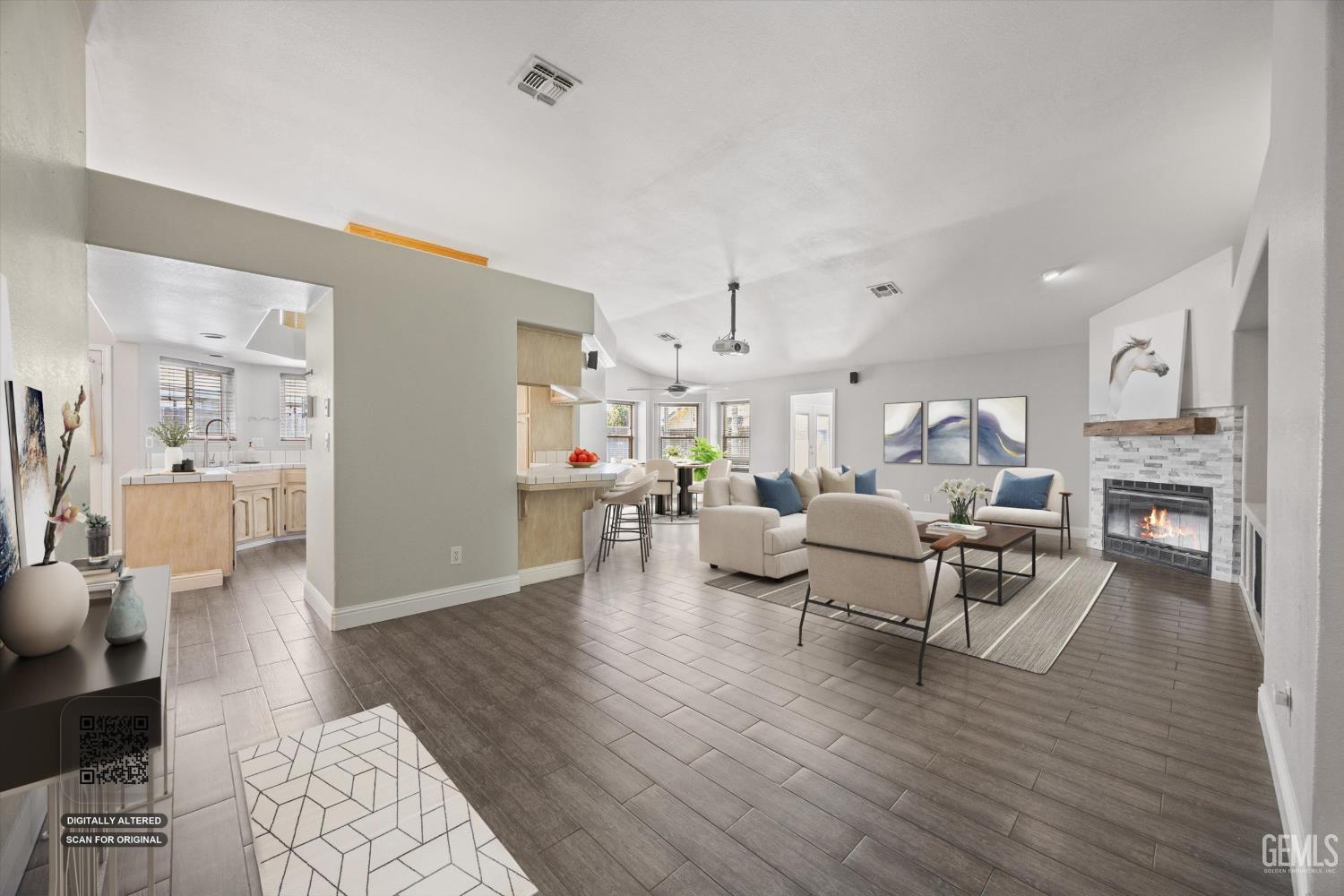 Staged open-plan living room with a tiled fireplace, light seating, and the kitchen island beyond.