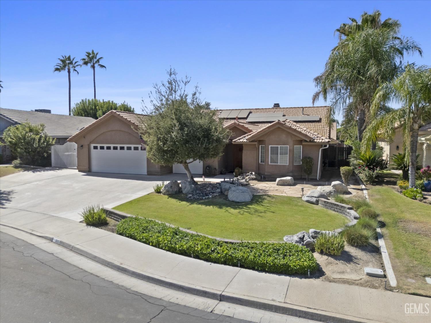 Single-story stucco home with solar panels, an attached garage, and a landscaped front yard.