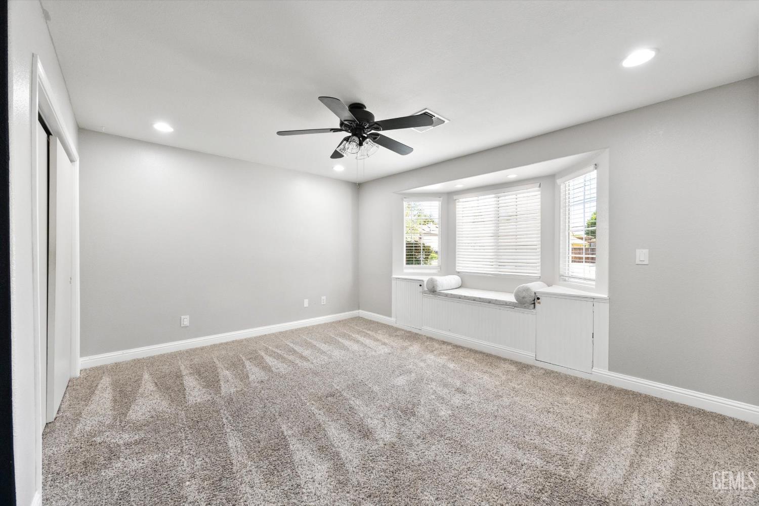 Empty bedroom with beige carpet and a built-in window seat beneath three windows.