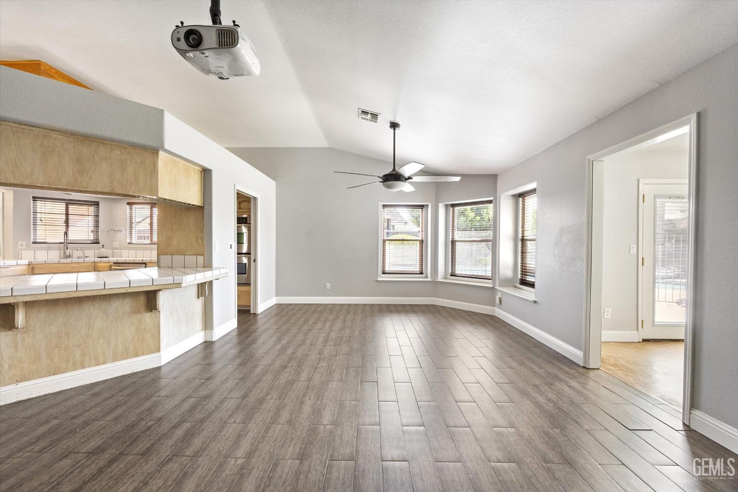 Open living and dining area with gray tile floors, a kitchen counter, three windows, and a ceiling fan.