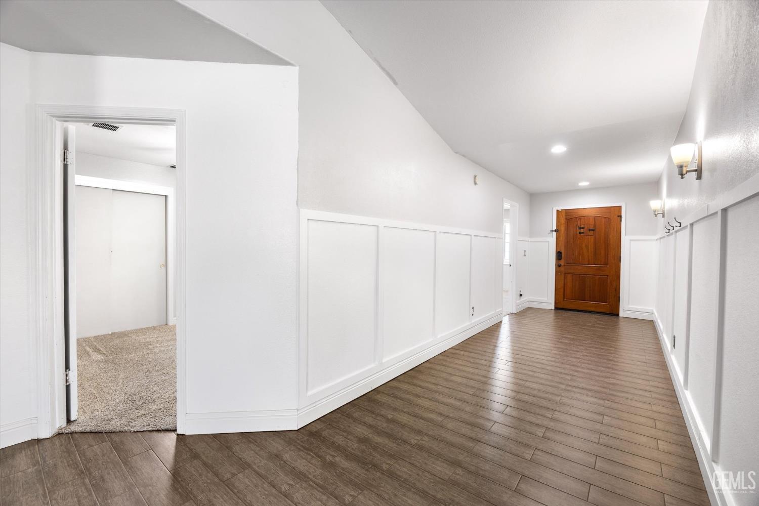 Hallway with white paneled walls, brown tile flooring, and a wooden front door.