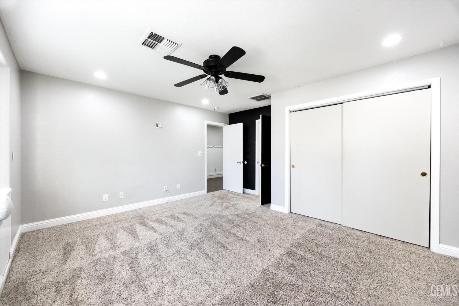 Empty carpeted bedroom with sliding closet doors and a black ceiling fan.