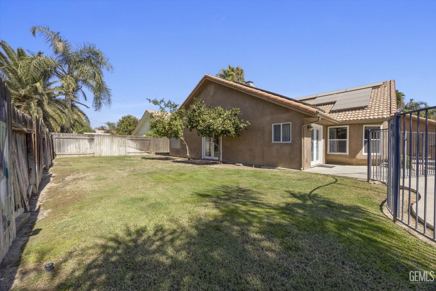 Home’s rear exterior and fenced grassy backyard, with solar panels and a concrete patio.