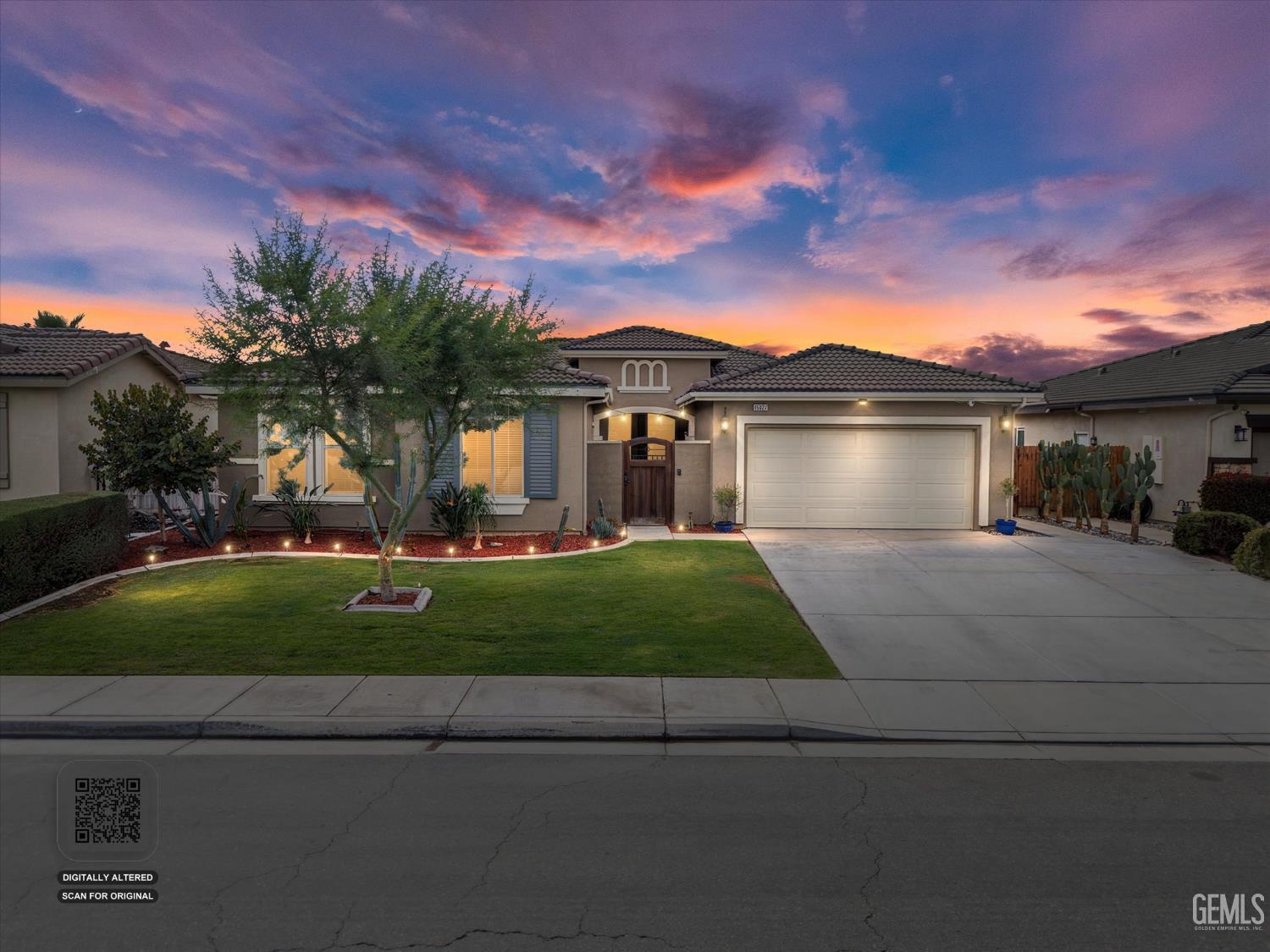 Single-story stucco home with a double garage and landscaped lawn beneath a vivid sunset sky.