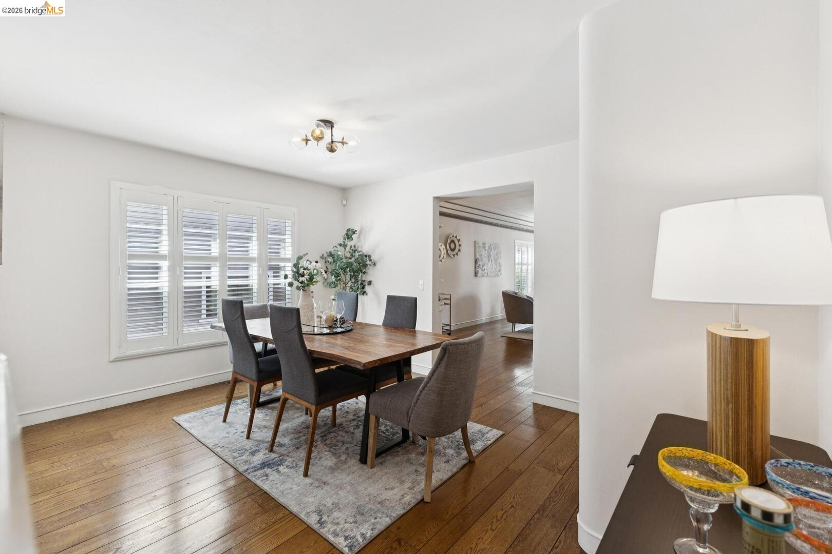 Dining room with a dark wood table, upholstered chairs, shuttered windows, and hardwood floors.