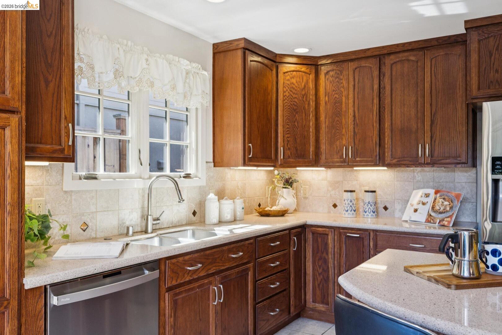 Kitchen with dark wood cabinets, light countertops, tiled backsplash, and a sink beneath two windows.