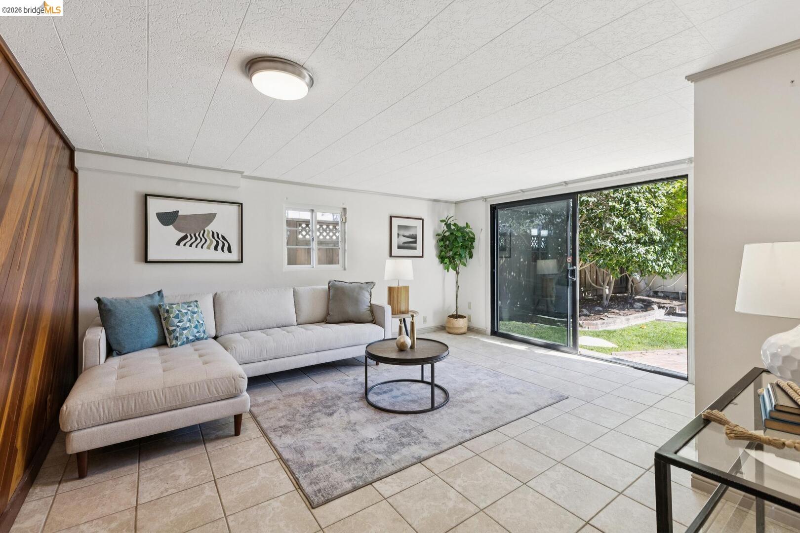 Living room with a light sectional sofa and sliding glass door opening to a garden.