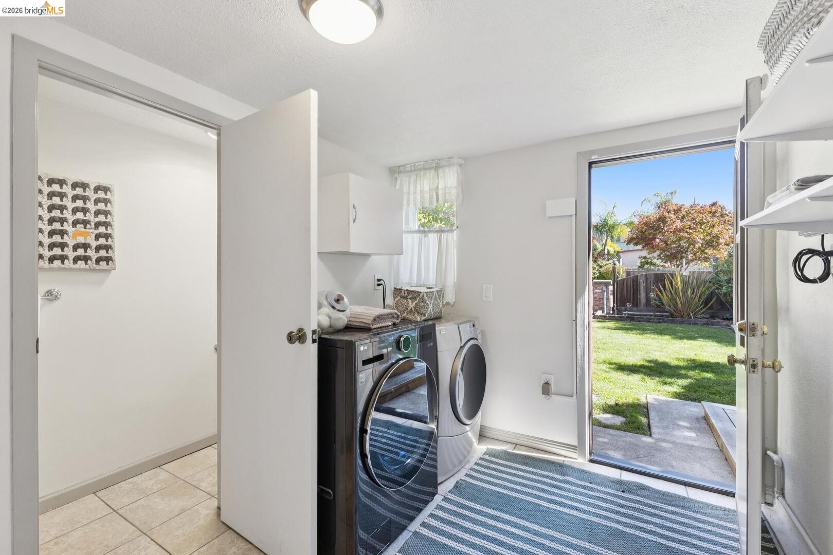 Laundry room with front-loading washer and dryer beside an open doorway to the backyard.