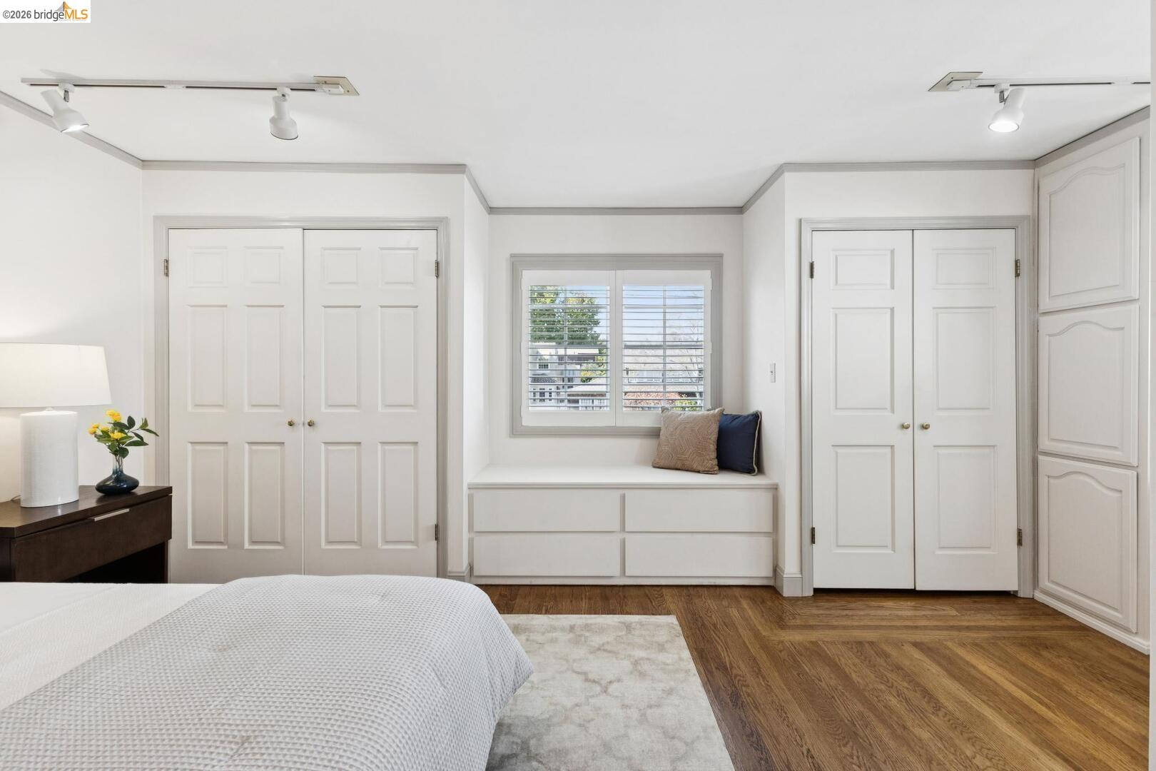 Staged bedroom with a built-in window seat, plantation shutters, paneled doors, and hardwood floors.