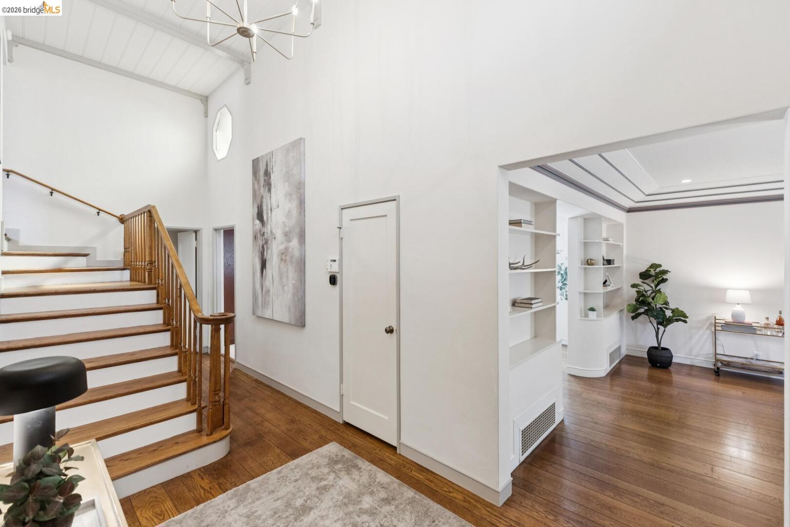 Entry hall with a wood staircase, hardwood floors, and an adjoining sitting room with built-in shelves.