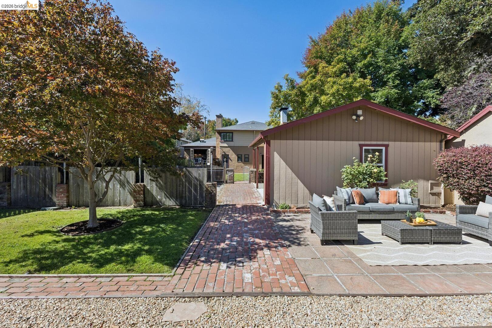 Backyard patio with wicker seating beside a brick walkway and mature tree.