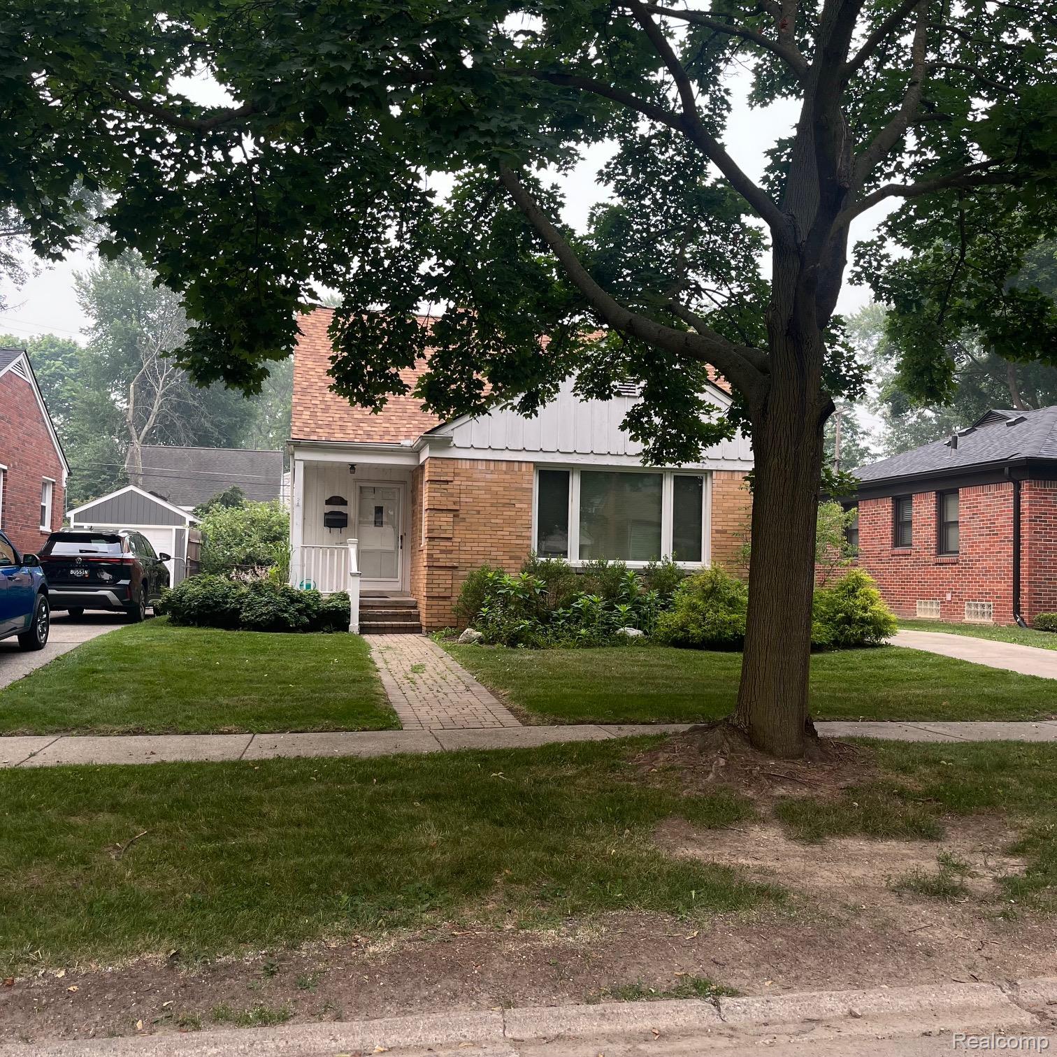 Brick house with a white entry and large shade tree over the front lawn and walkway.