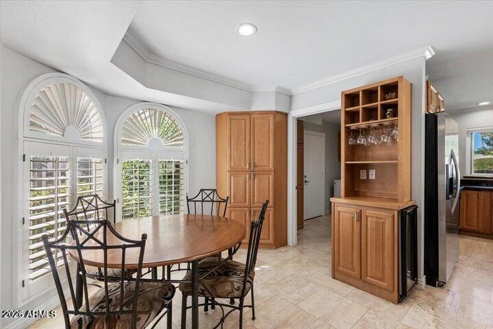 Dining area with an oval wooden table, arched shuttered windows, and a built-in wooden cabinet.