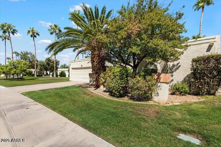 Stucco home with garage, landscaped lawn, palms, and mature trees along a Scottsdale sidewalk.