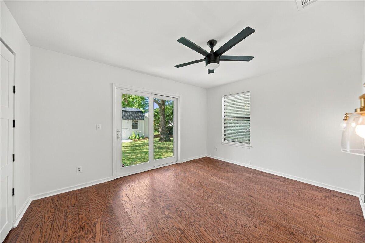 Unfurnished room with hardwood floors, a black ceiling fan, and a sliding glass door to the yard.