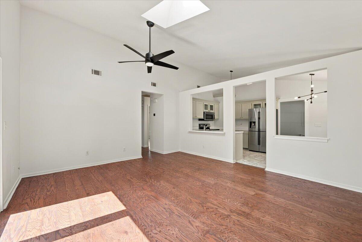 Empty living room with hardwood floors, a high ceiling, and pass-through openings to the kitchen.