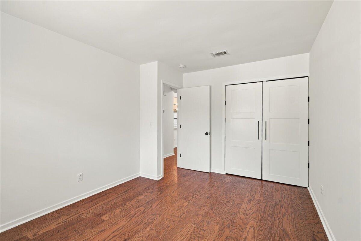 Empty bedroom with reddish hardwood floors and a double-door closet.