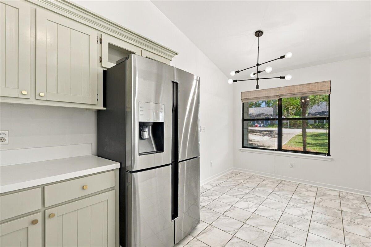 Kitchen with pale cabinets, a stainless steel refrigerator, marble-look tile flooring, and a window overlooking greenery.