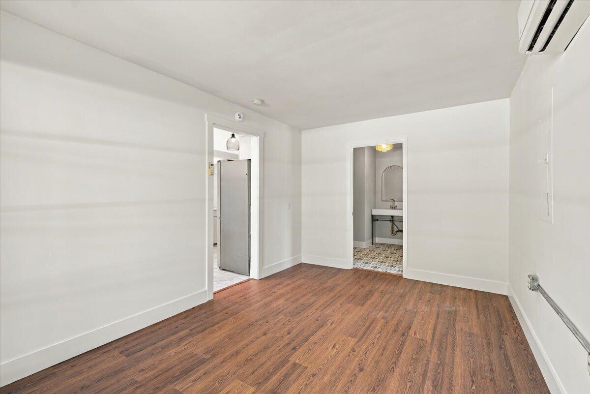 Empty room with reddish-brown wood floors, opening to a small bathroom and adjoining space.