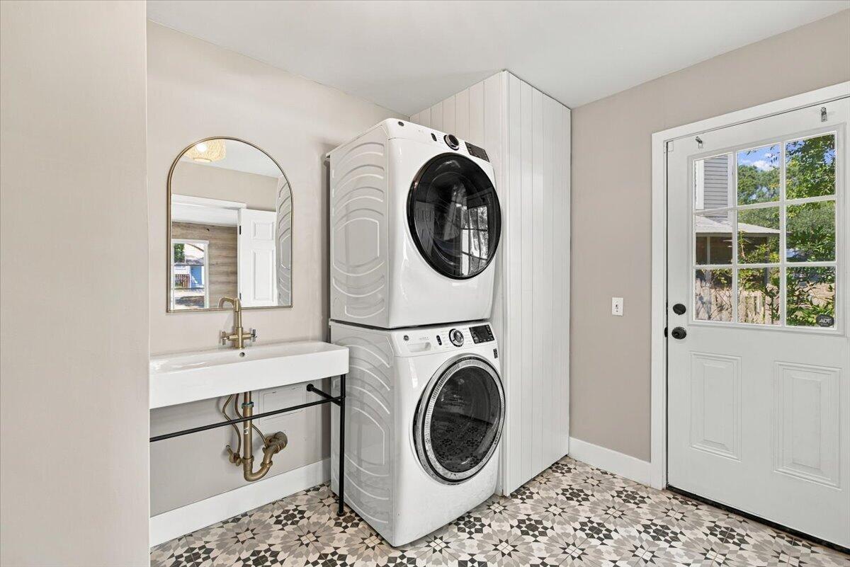 Laundry room with stacked washer and dryer, utility sink, arched mirror, and patterned tile floor.