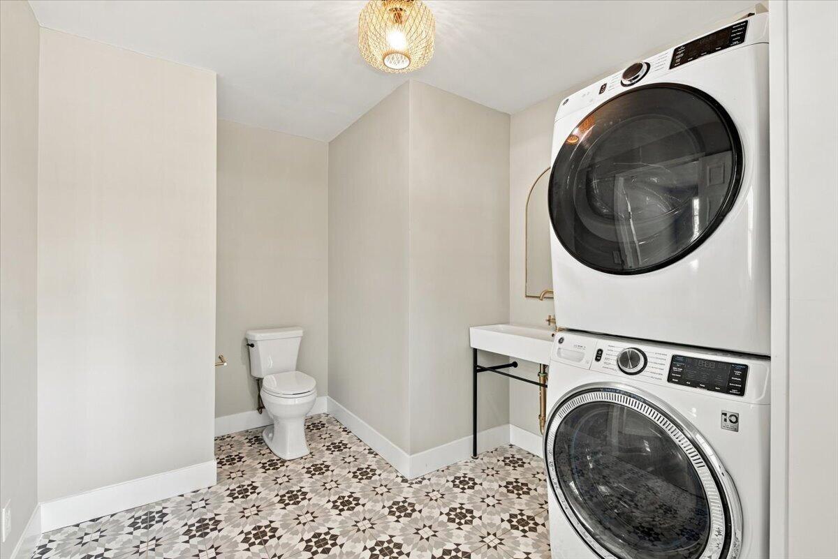 Laundry room with stacked washer and dryer, utility sink, toilet, and patterned tile floor.